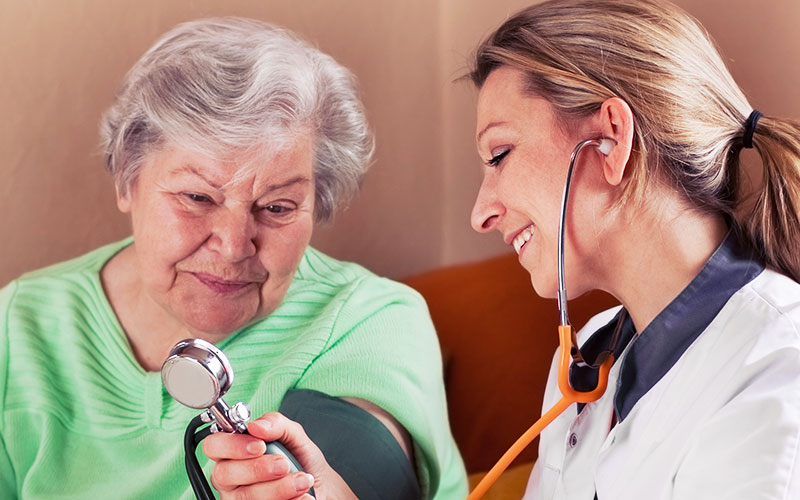 Pflegehelferin misst Blutdruck bei einer Seniorin
